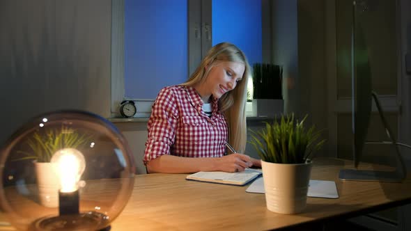 Smiling Woman Working on Computer at Night. Smiling Female in Checkered Shirt Sitting at Lit By