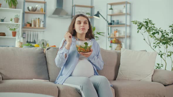 Pregnant Woman With Great Pleasure Eating Vegetable Salad on the Couch