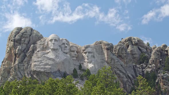 Looking past pine trees towards Mount Rushmore as clouds move overhead