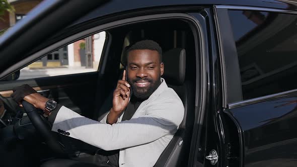 African American Man in white Jacket Sitting at the Driver's Seat and Talking on Mobile