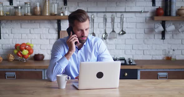 Businessman Looking in Laptop and Talking Phone at Home