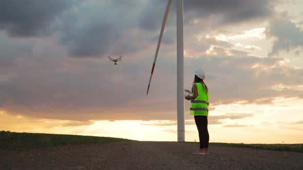 Woman Professional engineer in uniform holding joystick controlling fly drone work windmill sunset