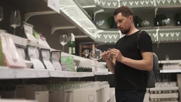 a Young Man Chooses Beautiful Glasses in the Mall for His New Apartment