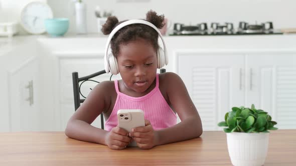 Charming Little Girl Wearing Wireless Headphones Using Smartphone Listens to the Music Watching