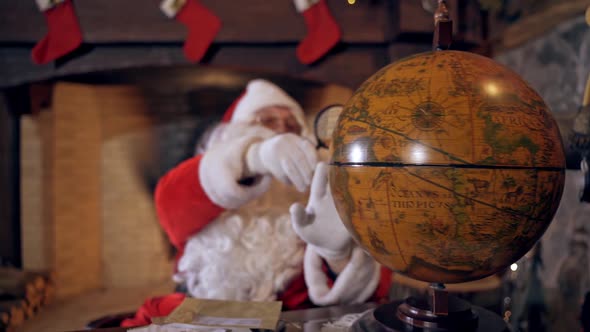 Santa looking at the globe. Santa Claus is sitting and turning the model of the globe.