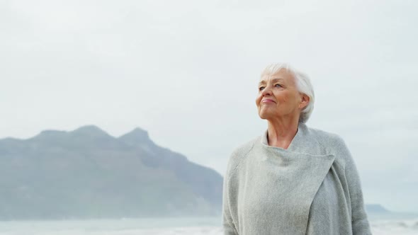 Senior woman standing with hands raised on beach