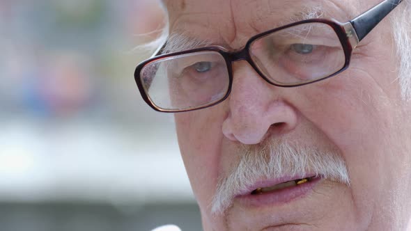 Upset Grandfather with Glasses He is Sitting Pensively in the Park on a Bench