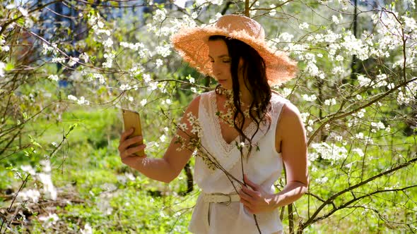 Brunette Woman with Long Hair in a Straw Hat Stands in the Apple Orchard