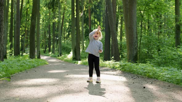 Cheerful Child in Striped Tshirt Waves Her Hand at Camera on Summer Sunny Day in Park Among Tall