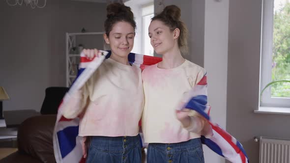 Medium Shot Smiling Adult Twin Sisters Wrapping in British Flag Hugging Looking at Camera