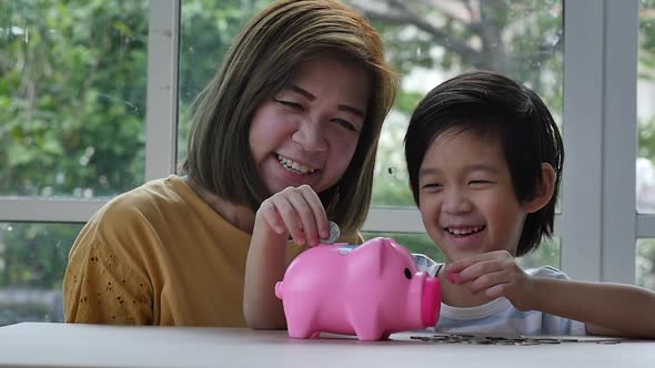 Cute Asian Child And Mother Putting A Coin In To A Piggy Bank