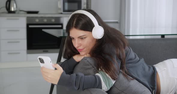 Teenage Girl Listening to Music Wearing Headphones Relaxing on Sofa Texting Using Smartphone