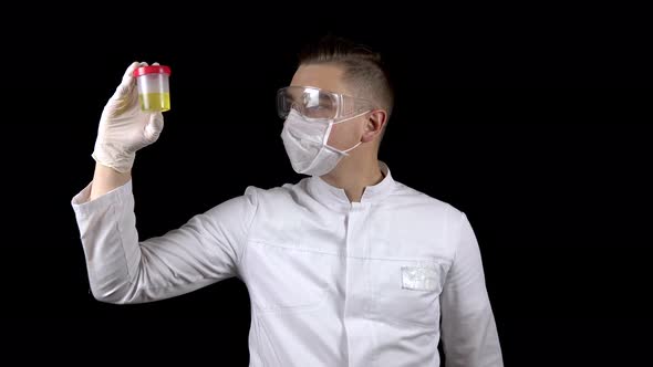 A Young Man Doctor Is Checking Urine Tests. A Man Examines a Test Jar Containing Urine on a Black