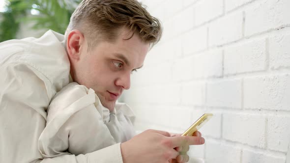 Tired Businessman Lies in Bed in White Shirt and Works or Trades Stocks on Phone