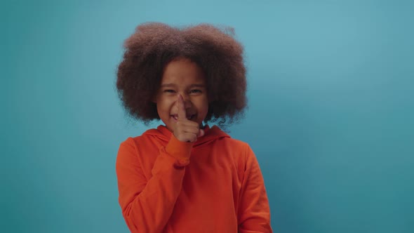 African American girl making silence gesture with forefinger by mouth