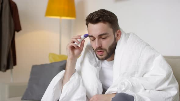 Sick Man Measuring Temperature with Forehead Thermometer