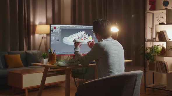 Male Footwear Designer Holding And Looking At The Colourful Pattern Sneakers While Designing Shoe