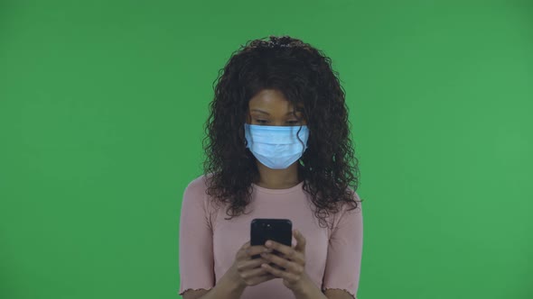 Portrait of Beautiful African American Young Woman in Medical Mask Is Texting on Her Phone. Burning