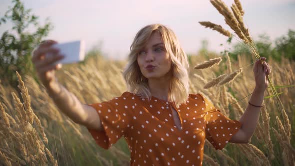 Attractive Fun Hippie Blonde Woman in the Field at Sunset Making a Selfie with a Bouquet