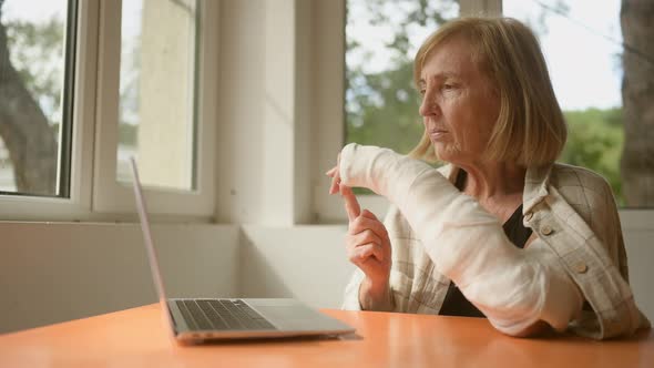 Senior Elderly Woman Having Video Chat Conference with Laptop Computer with Injury Broken Arm in