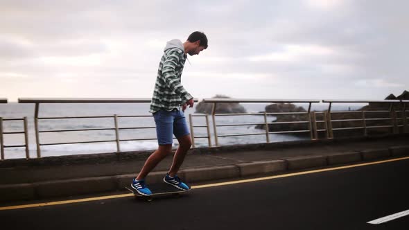 Sport Lifestyle Extreme and People Concept Tall Guy Riding Longboard By the Coastline Road in Cloudy