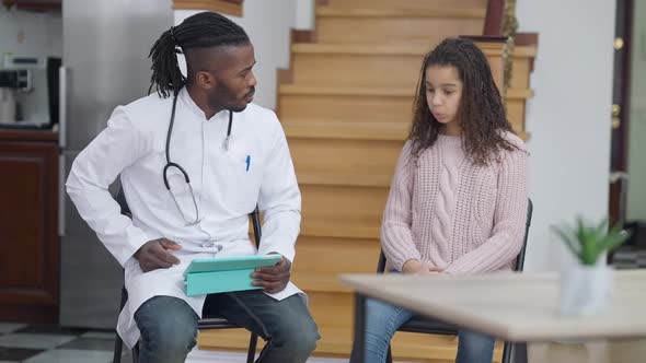 Family Doctor Visiting Teenage African American Girl at Home Checking Patient