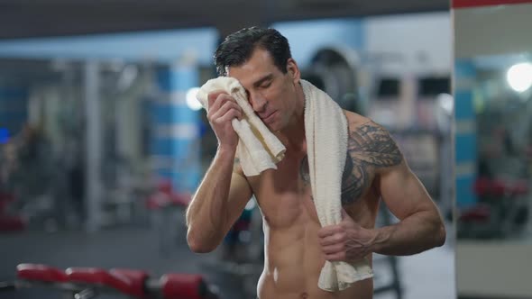 Portrait of Satisfied Tattooed Sportsman Wiping Sweat with Towel Looking at Camera Smiling and