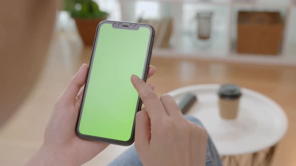 Woman holding mockup smartphone green screen with type message on the sofa at home.