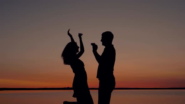 Silhouette Of A Happy Couple Give Hands Five At Sunset By The Coast