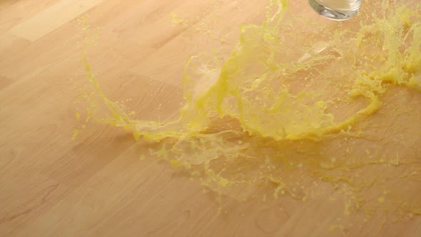 Dropping Glass of orange juice and breaking on wooden floor, Slow Motion