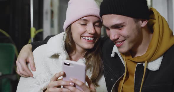 Handsome Guy Embracing His Lovely Girlfriend While They Looking at Smartphone Screen. Happy Young