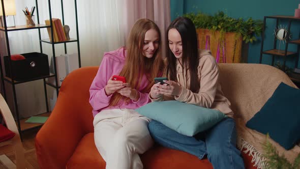 Cheerful Girls Friends Siblings Watching Photos on Smartphone on Sofa at Home Enjoy Social Media