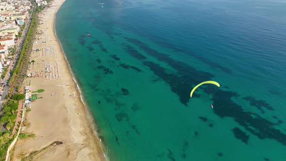 Aerial drone view of parachute jumper flying over beautiful beach