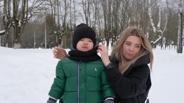 Mom Straightens the Hat and Scarf of Her Little Son