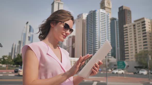 A Girl of European Appearance Works with a Tablet on the Background of Dubai Skyscrapers.