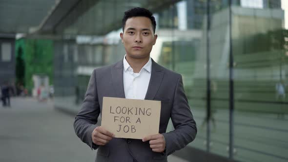 Real Time Portrait Shot of a Young Asian Man in a Suit Standing on the Street with a Sign "Hire Me"