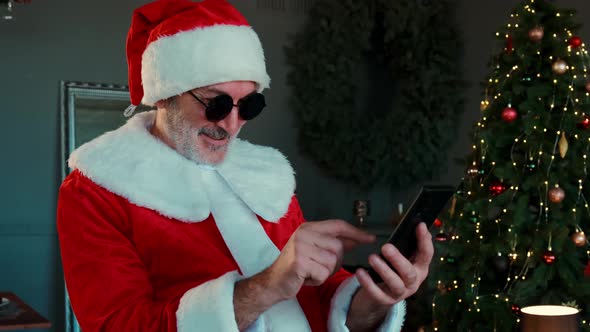 Cheerful Man Black Glasses Santa Claus Suit Is Sitting Living Room Chatting By Smartphone Video Chat