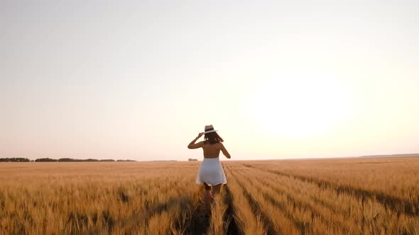 Happy Free Young Woman Runs in Slow Motion Across Field Touching Ears of Wheat with Her Hand