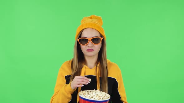 Portrait of Modern Girl in Yellow Hat in 3D Glasses Is Watching a Boring Movie and Eating Popcorn