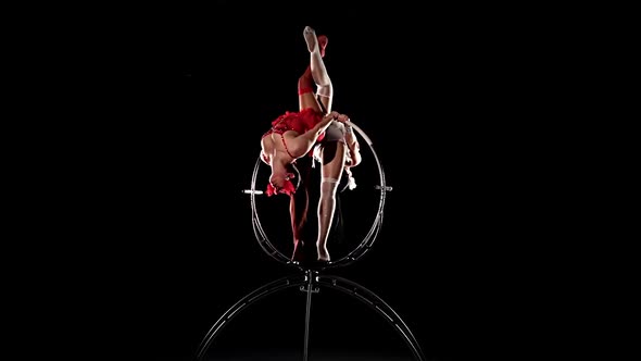 Two Gymnasts Performs a Trick on the Aerial Hoop Metal Construction. Black Background. Slow Motion
