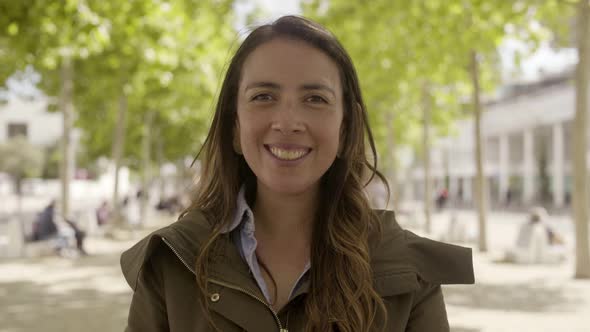 Smiling Young Woman Standing on Street and Blowing Air Kiss