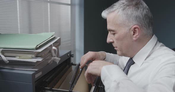 Corporate businessman searching for files in the filing cabinet