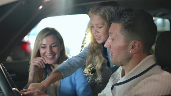 Happy Father Showing Car Dashboard to Curios Cute Daughter with Blurred Mother Smiling at Background