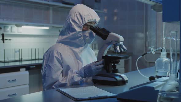 Epidemiologist in Protective Coveralls Using Microscope in Lab