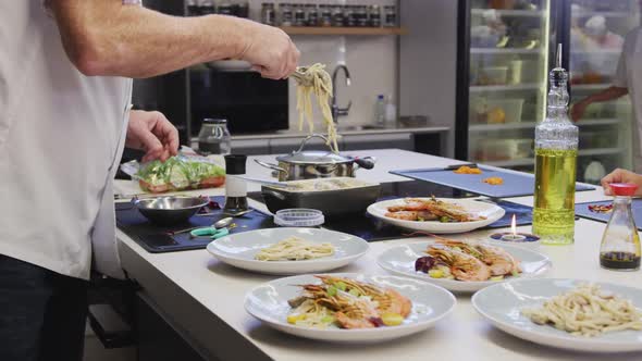 Caucasian male chef wearing chefs whites in a restaurant kitchen, putting food on a plate