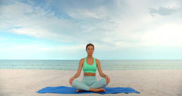 Sport Woman Seats on Yoga Mat in Lotus Pose and Meditating She Located Outdoors on the Beach