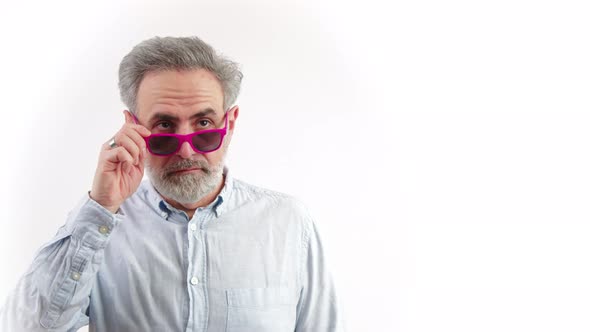 Elderly Grayhaired Bearded Caucasian Man in a Shirt Holding Pink Sunglasses and Looking Around