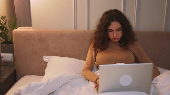 Pretty Caucasian Woman Working Laptop on Bed at Home