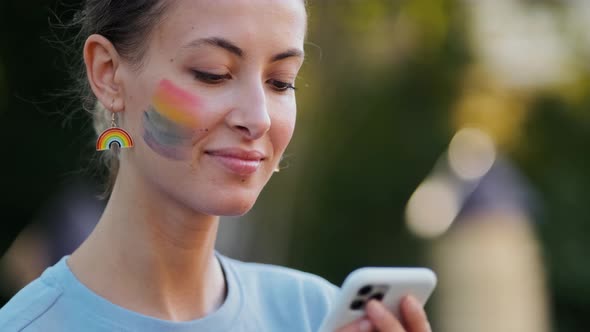 A close-up view of a pretty nice woman with rainbow make-up typing message using her phone during pr