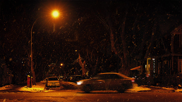 Cars Drive Past City Road With Snow Falling